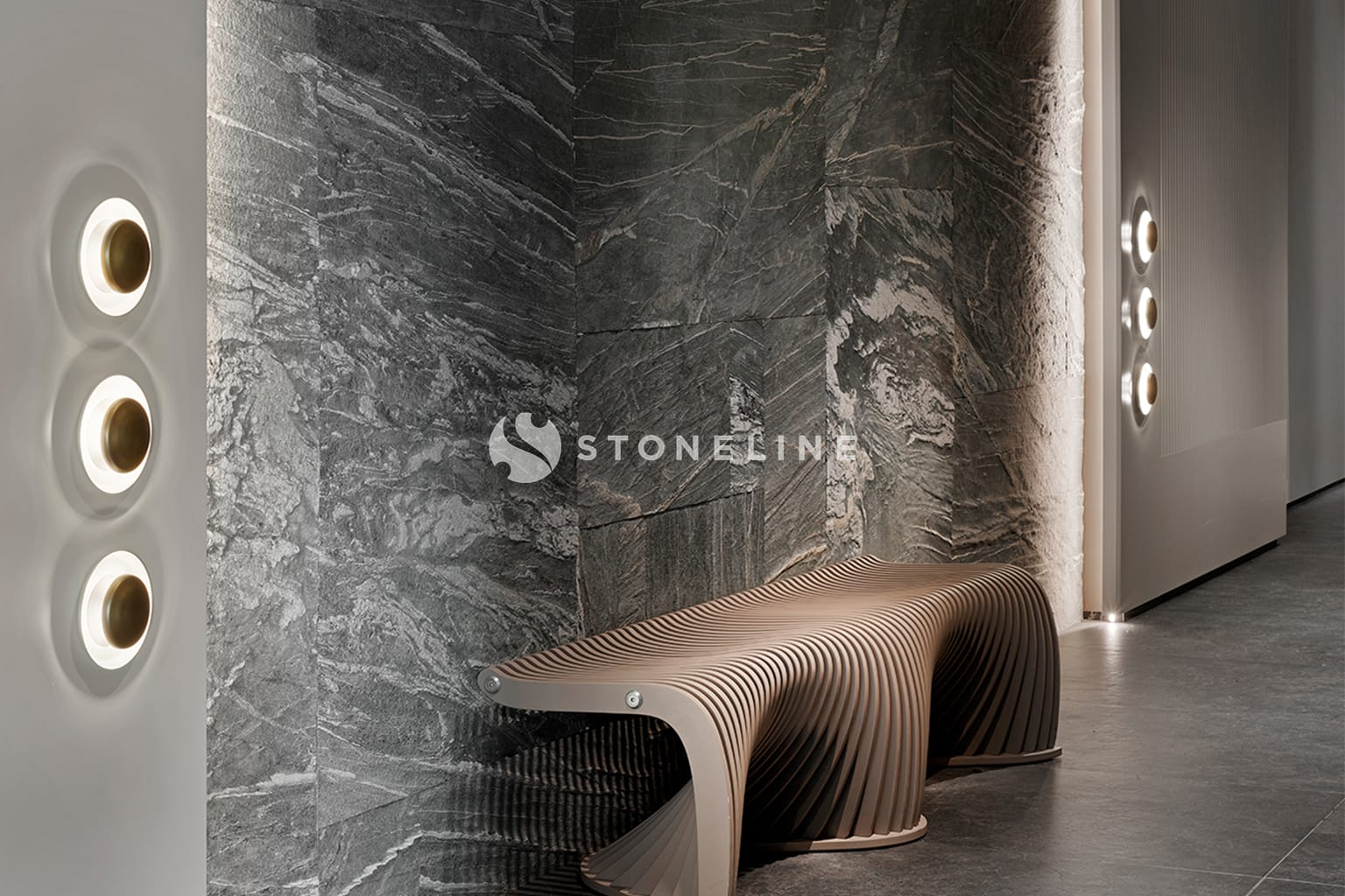 Modern bench beside textured stone wall with lights.